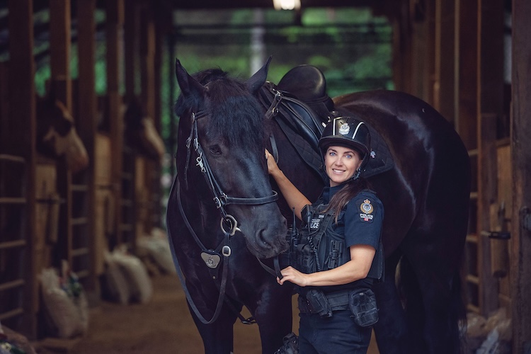 Three women in an office setting collaborate around a laptop, smiling and engaged in discussion.
