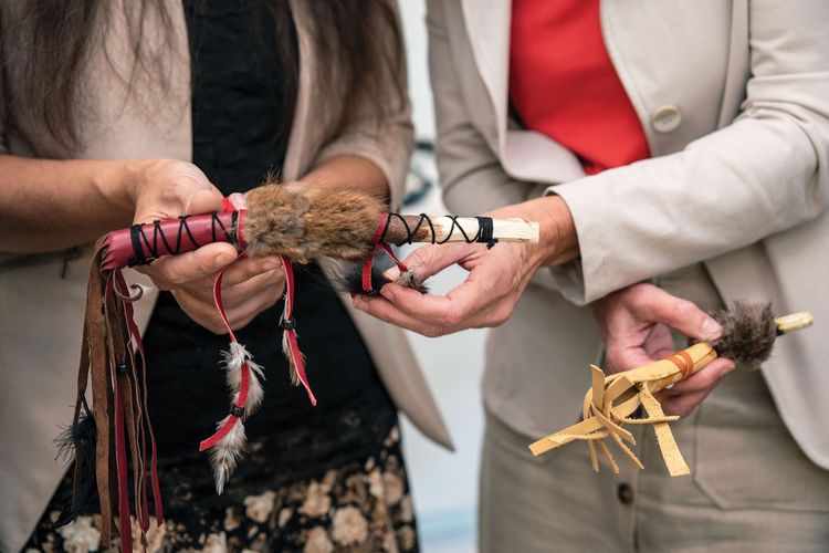 Three women in an office setting collaborate around a laptop, smiling and engaged in discussion.
