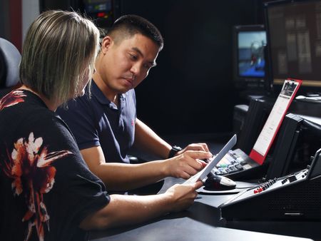 Two people focused on their work in a control room with multiple screens and broadcasting equipment.